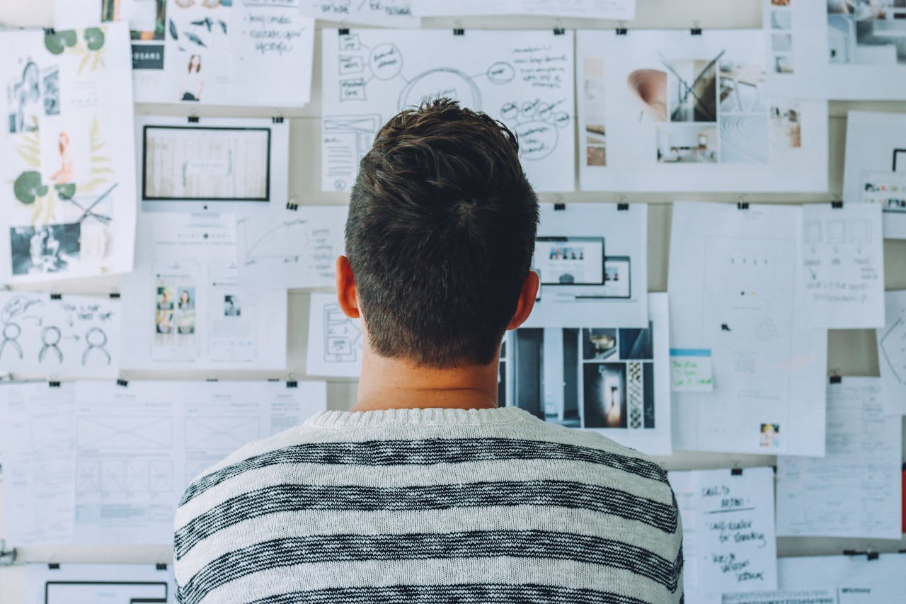 Man Wearing Black and White Stripe Shirt Looking at White Printer Papers on the Wall